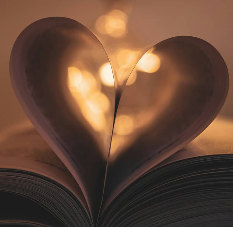 A book with pages folded into a heart shape against warm bokeh lights