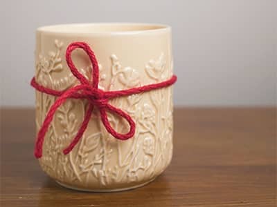 A solid, cream-colored candle jar with raised flowers and red bow.