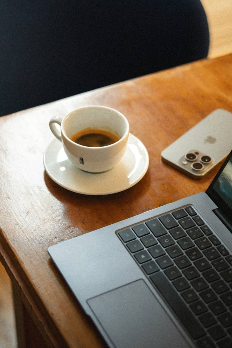 Coffee, phone, and laptop on a wooden table.