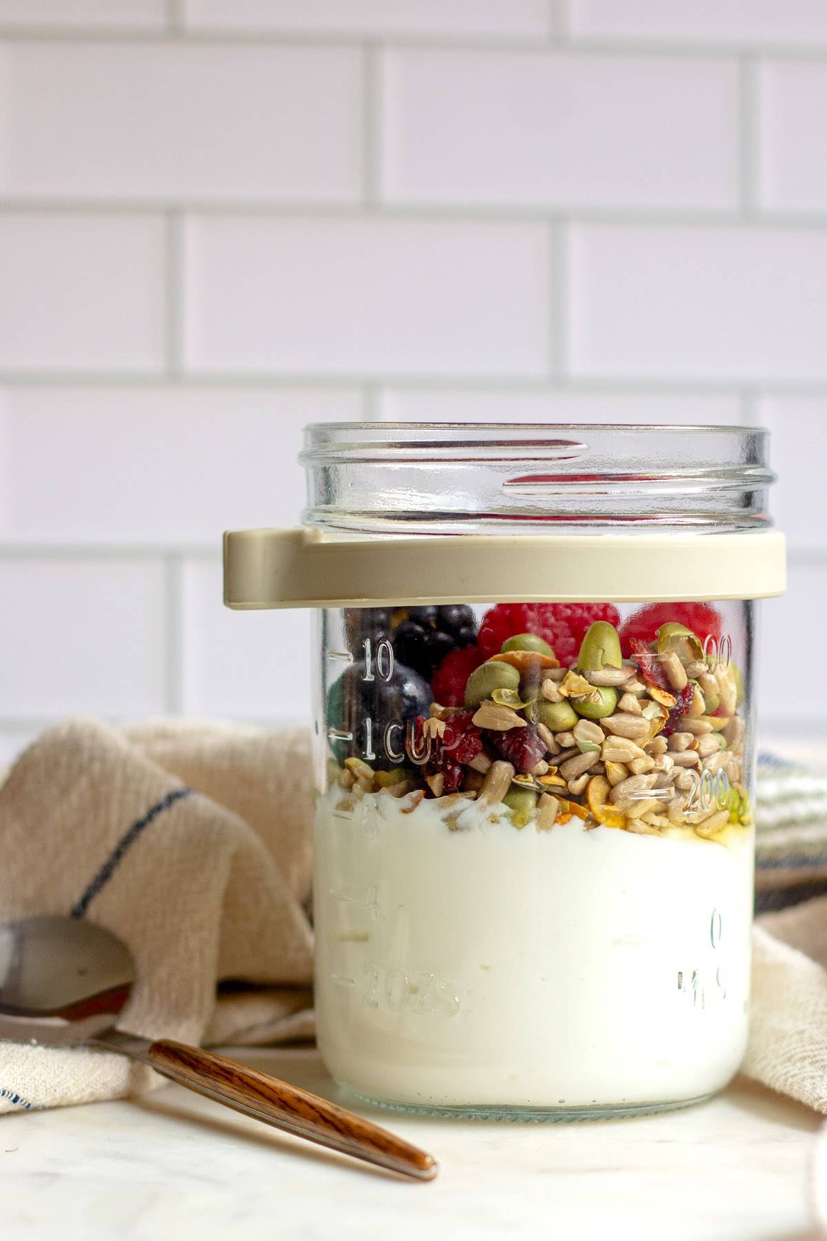 A layered Greek yogurt parfait in a clear glass jar filled with creamy yogurt, fresh strawberries and blueberries, sprinkled with chopped nuts, and lightly drizzled with honey.