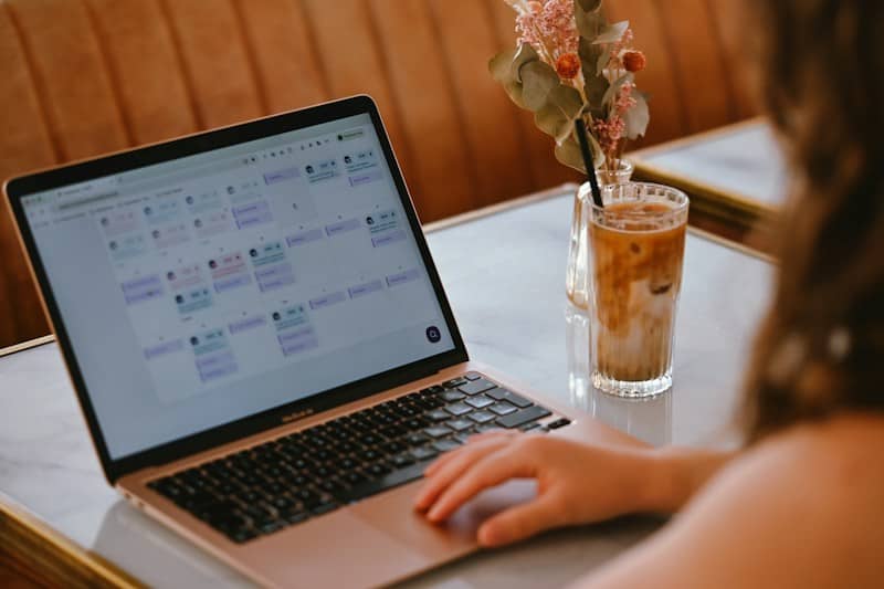 A person using a laptop with a calendar interface beside an iced coffee