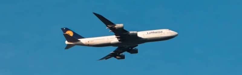 A plane flies high against a clear blue sky.