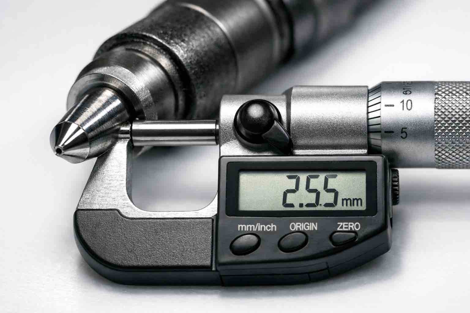 Fotografia macro de bico injetor de motor a diesel sendo medido por micrômetro, representando a perícia mecânica forense da Bruxel Perícias no RS