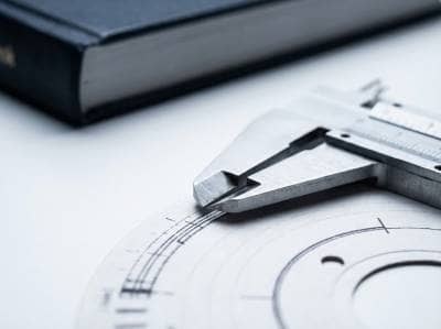 Fotografia macro de um disco de tacógrafo sobre mesa branca sendo medido com um paquímetro de aço inox, ilustrando a perícia de precisão realizada pela Bruxel Perícias no Litoral Norte gaúcho.