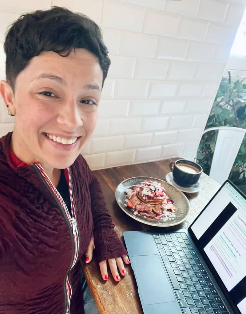 Quetzalli is sitting at a cafe shop writing her newsletter while she eat pancakes and coffee.