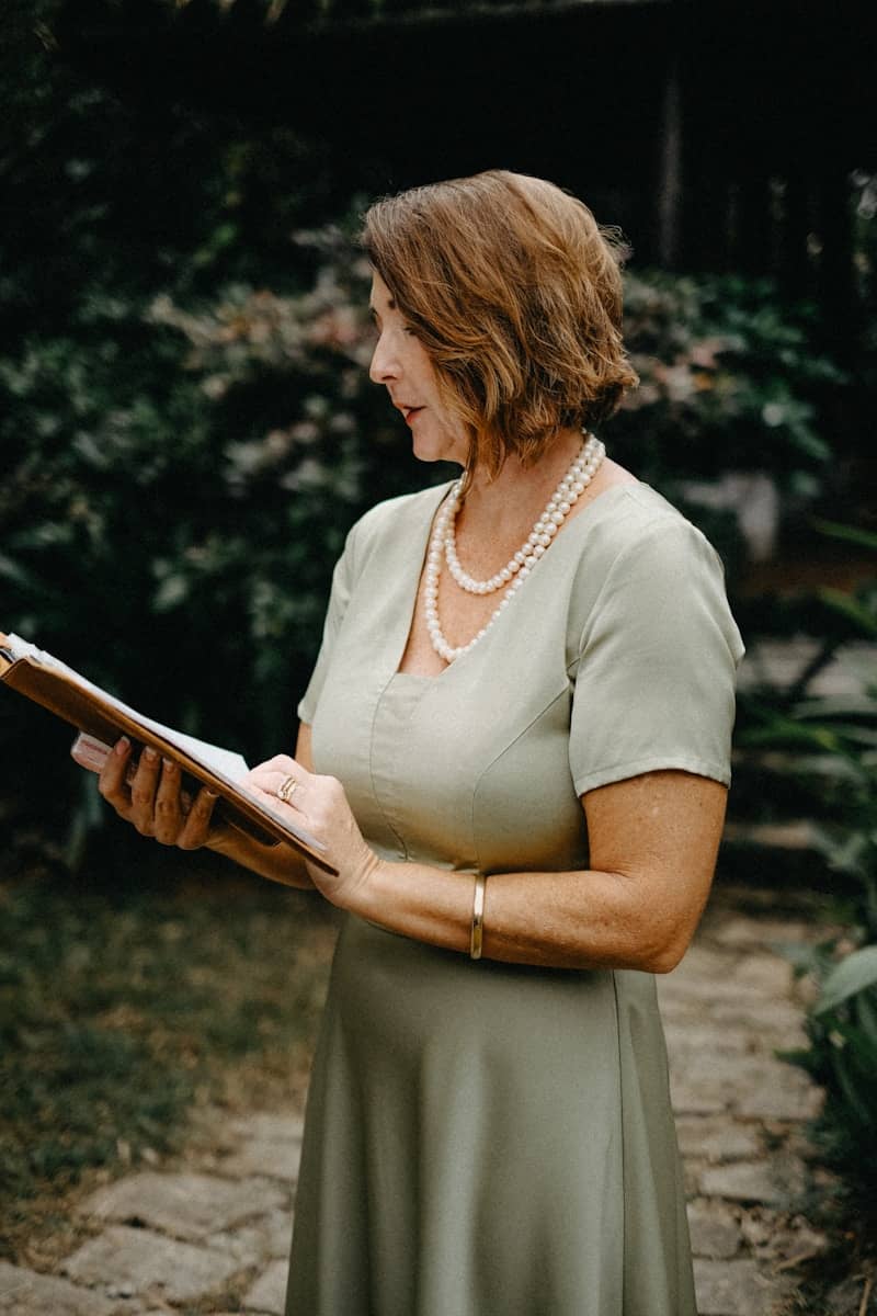 Woman in a pale green dress reading from a book.