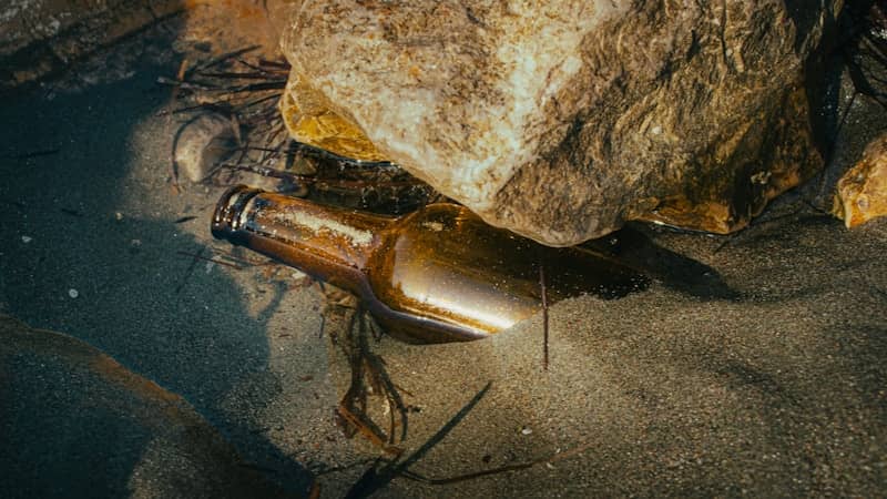 Brown glass bottle submerged in shallow water near a rock.