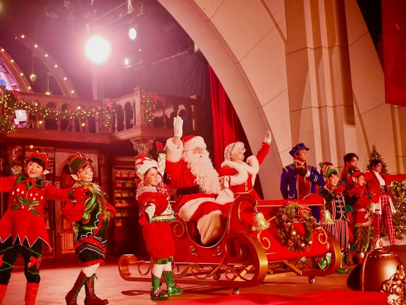 Santa claus and elves on a festive stage.