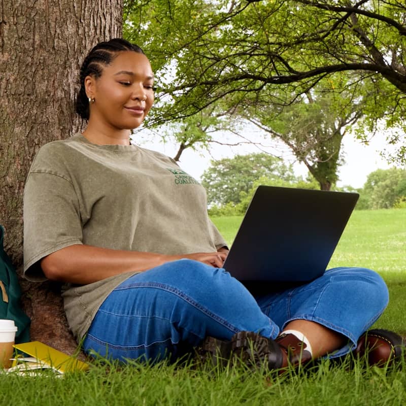 Woman using laptop while sitting under a tree