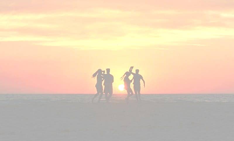 silhouette photo of four people dancing on sands near shoreline