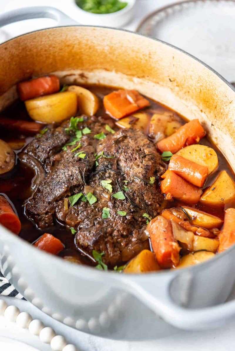 An image of Dutch Oven Pot Roast with carrost and potatoes and fresh herbs.