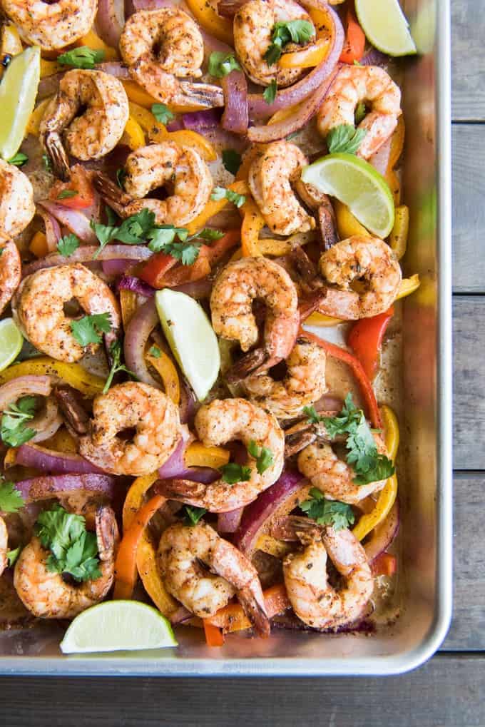 An image of sheet pan fajitas with shrimp, limes, peppers, and onions.