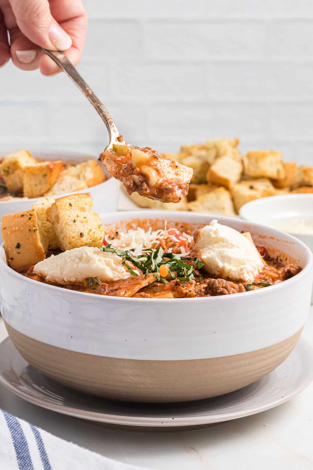 An image of cheesy lasagna soup with slices of bread.