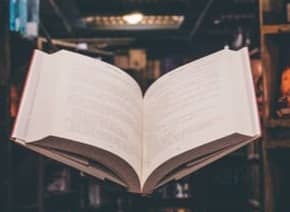 view of floating open book from stacked books in library