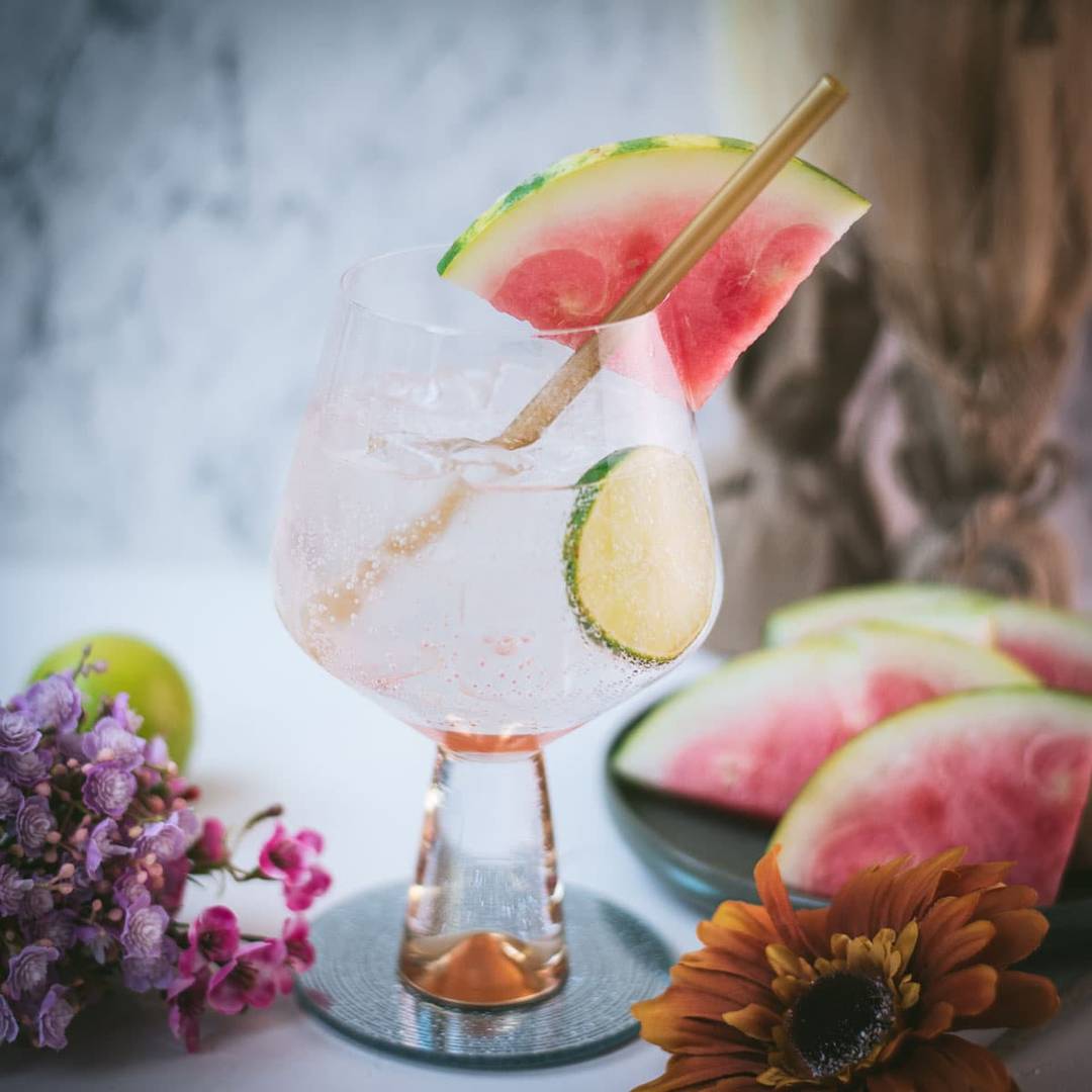 Watermelon gin and tonic with ice, watermelon pieces, and a fresh garnish, linking to the recipe.