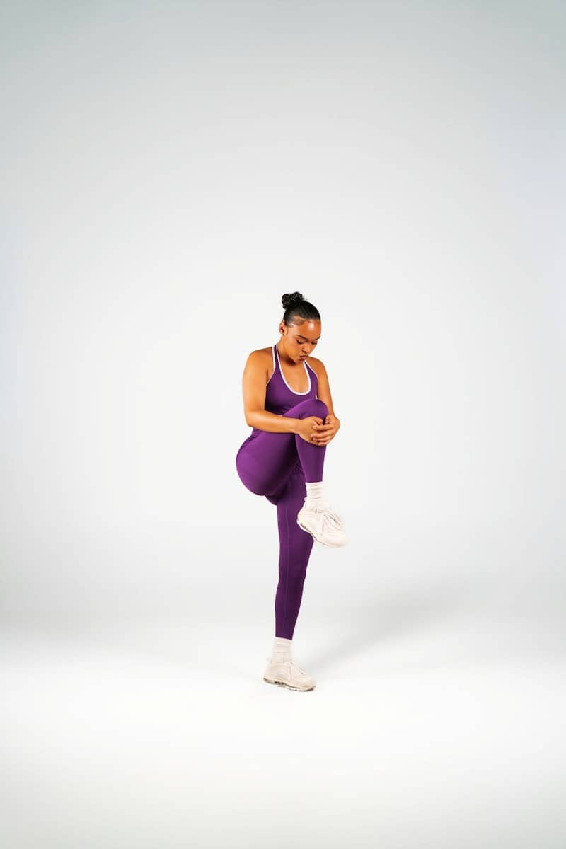 A woman in purple athletic wear stretching her leg against a white background