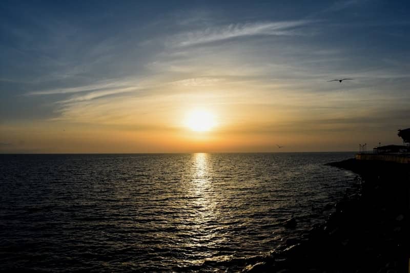 Sunset over a calm ocean with rocky shore.