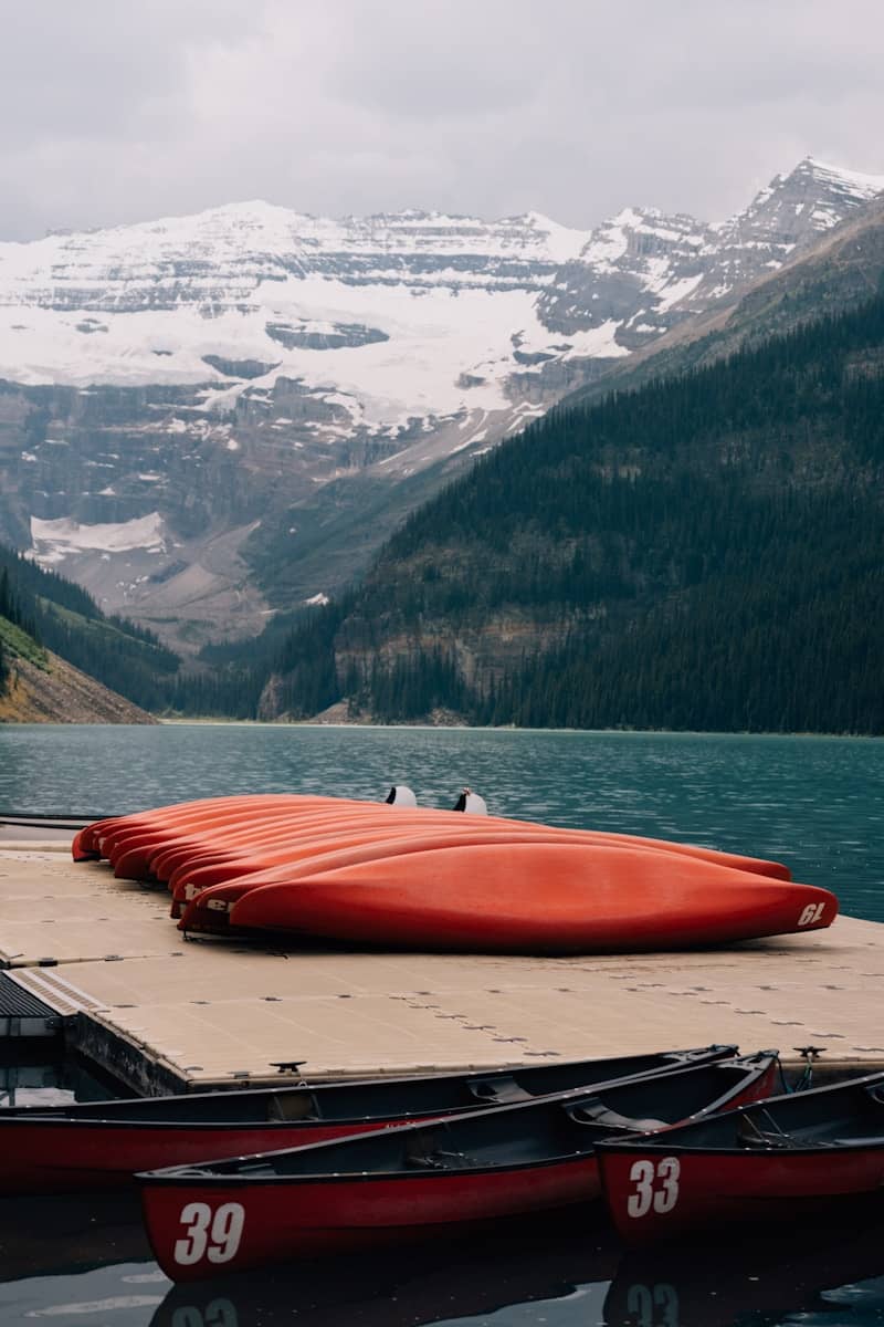 Red canoes are stacked near a mountain lake.