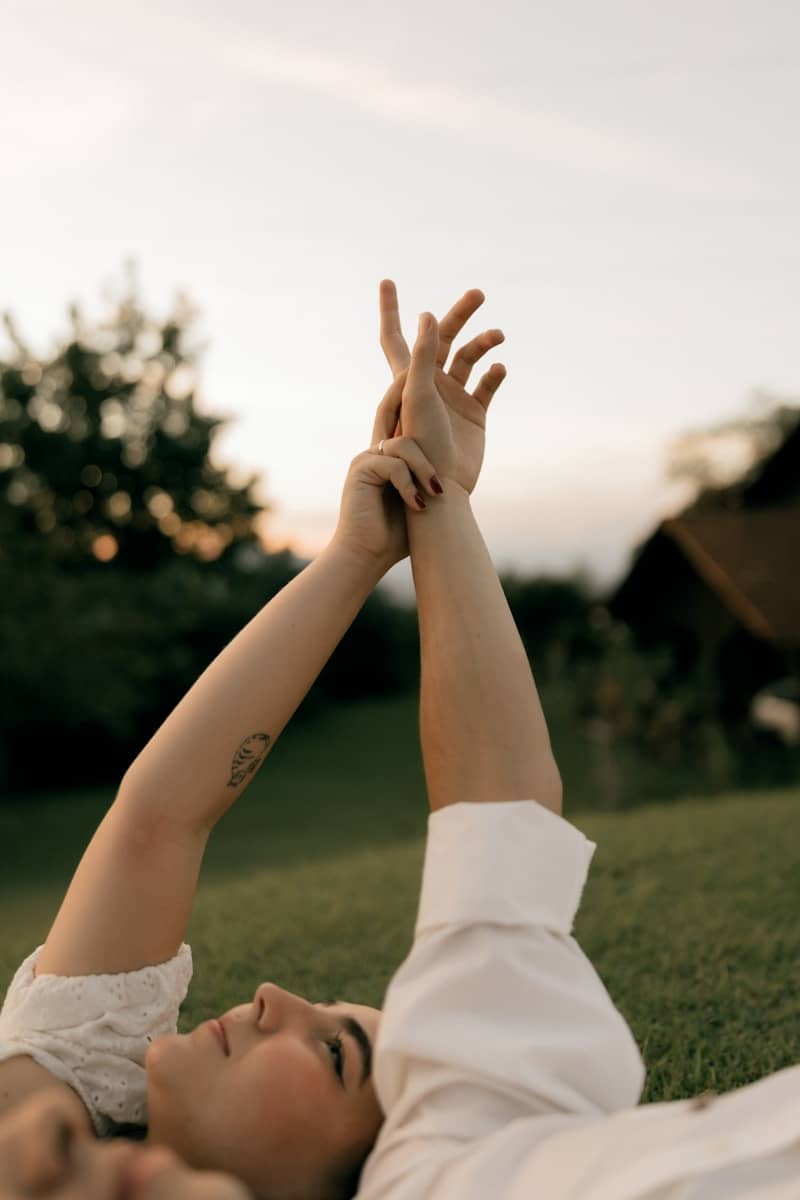 Woman lying on grass, hands intertwined against a sunset sky.