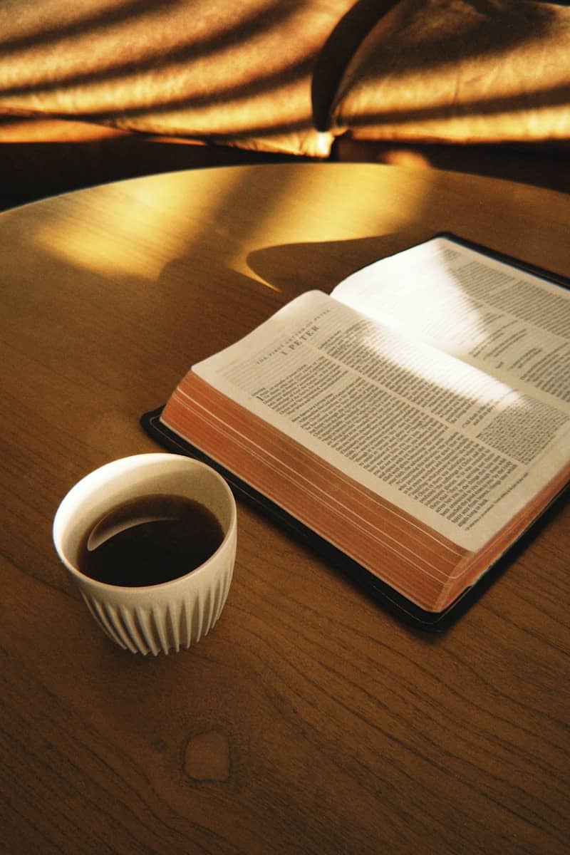 Open bible and coffee cup on a sunlit wooden table.