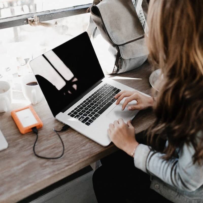 girl wearing grey long-sleeved shirt using MacBook Pro on brown wooden table