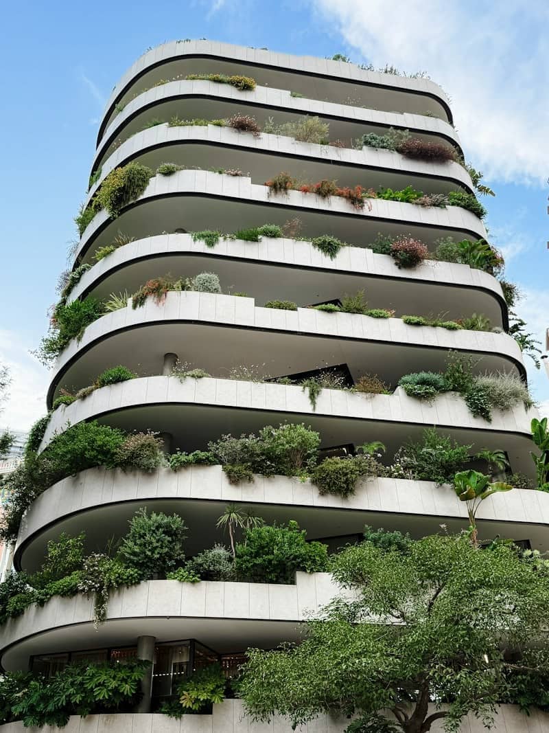 A modern residential building with curved white balconies overflowing with lush green plants