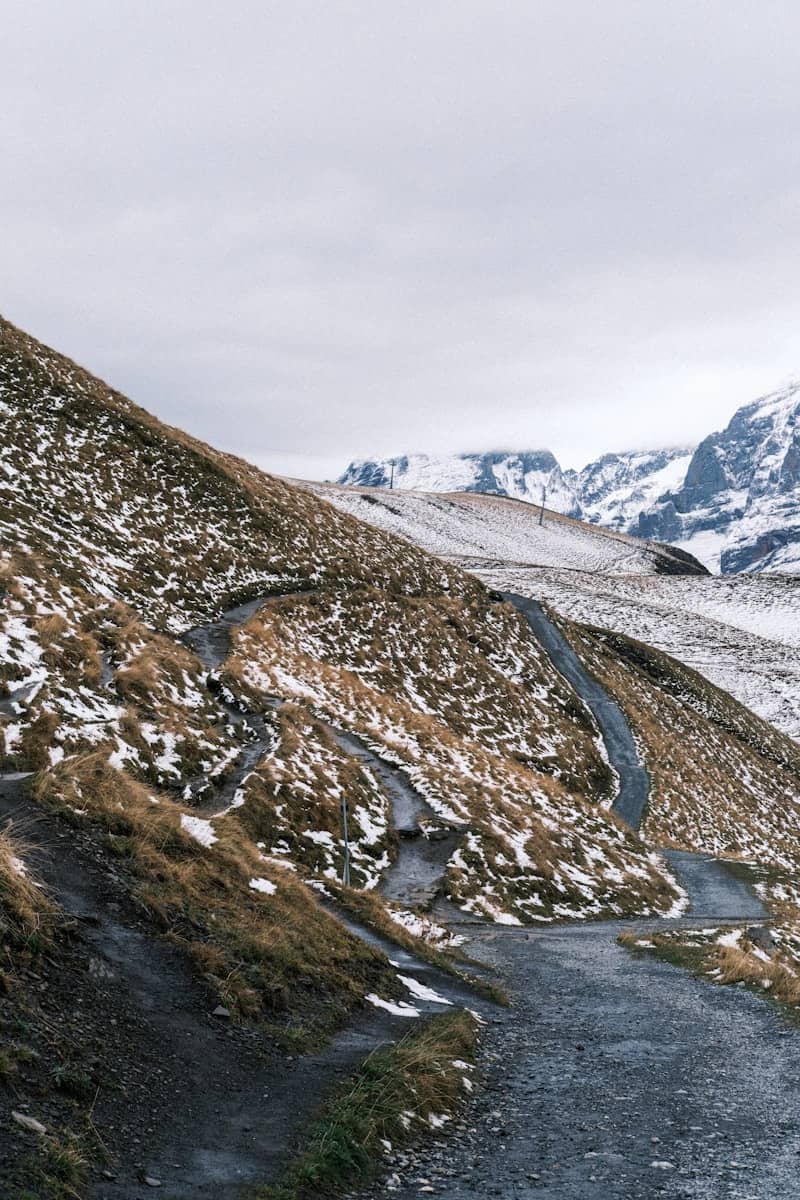 Winding mountain path through snowy, grassy hills