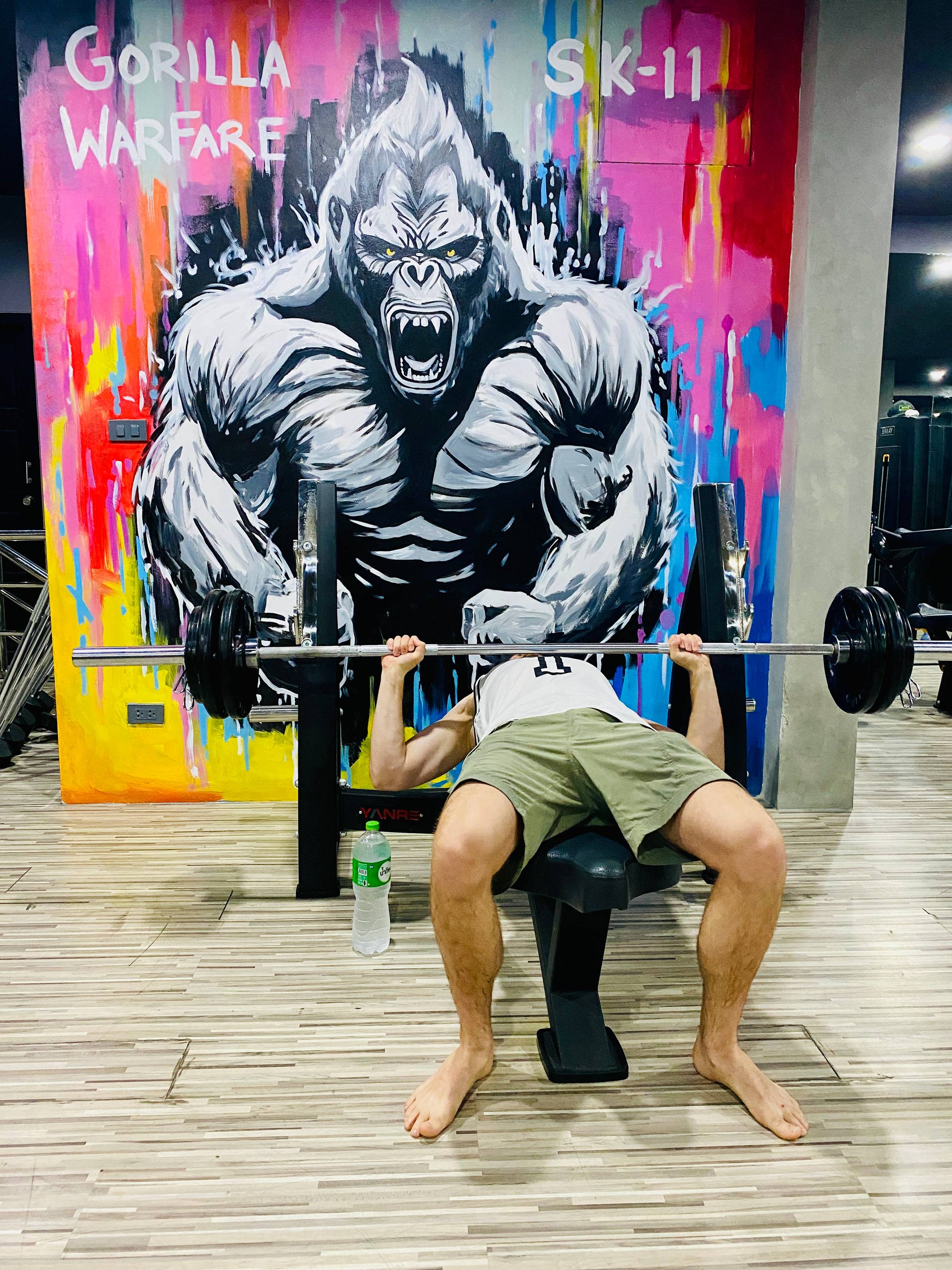 A man on the bench press machine in front of a graffiti gorilla.