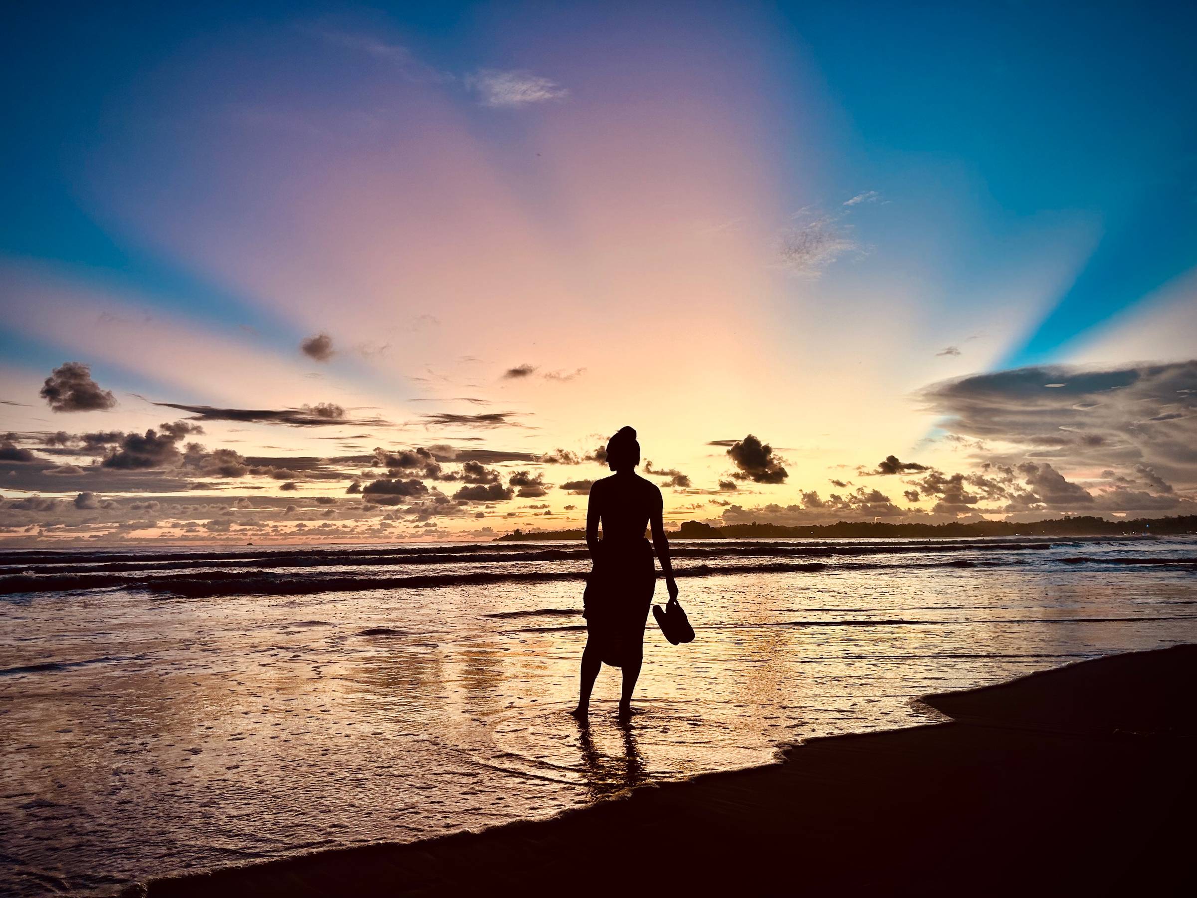 Woman silhouetted on a beach during a coourful sunset.