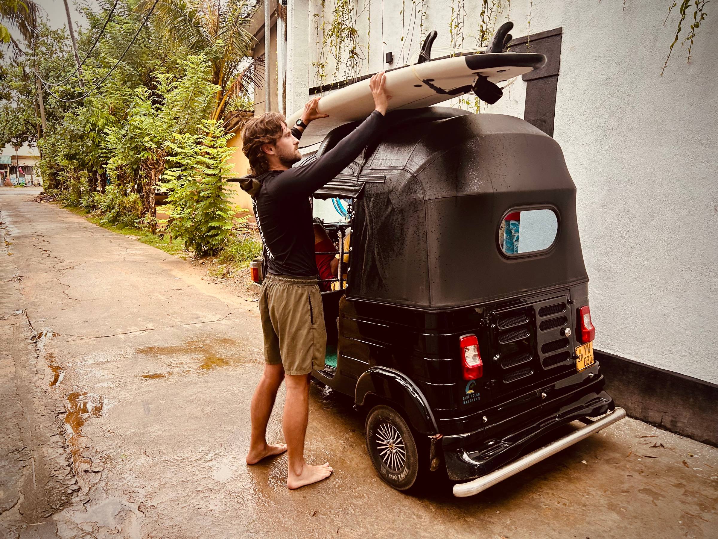 Man placing his surfboard on the rood of a tuk tuk in Sri Lanka.