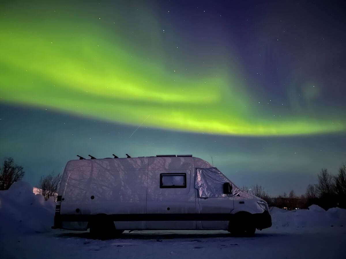 A campervan sat underneath the green glow of the northern lights in Norway.