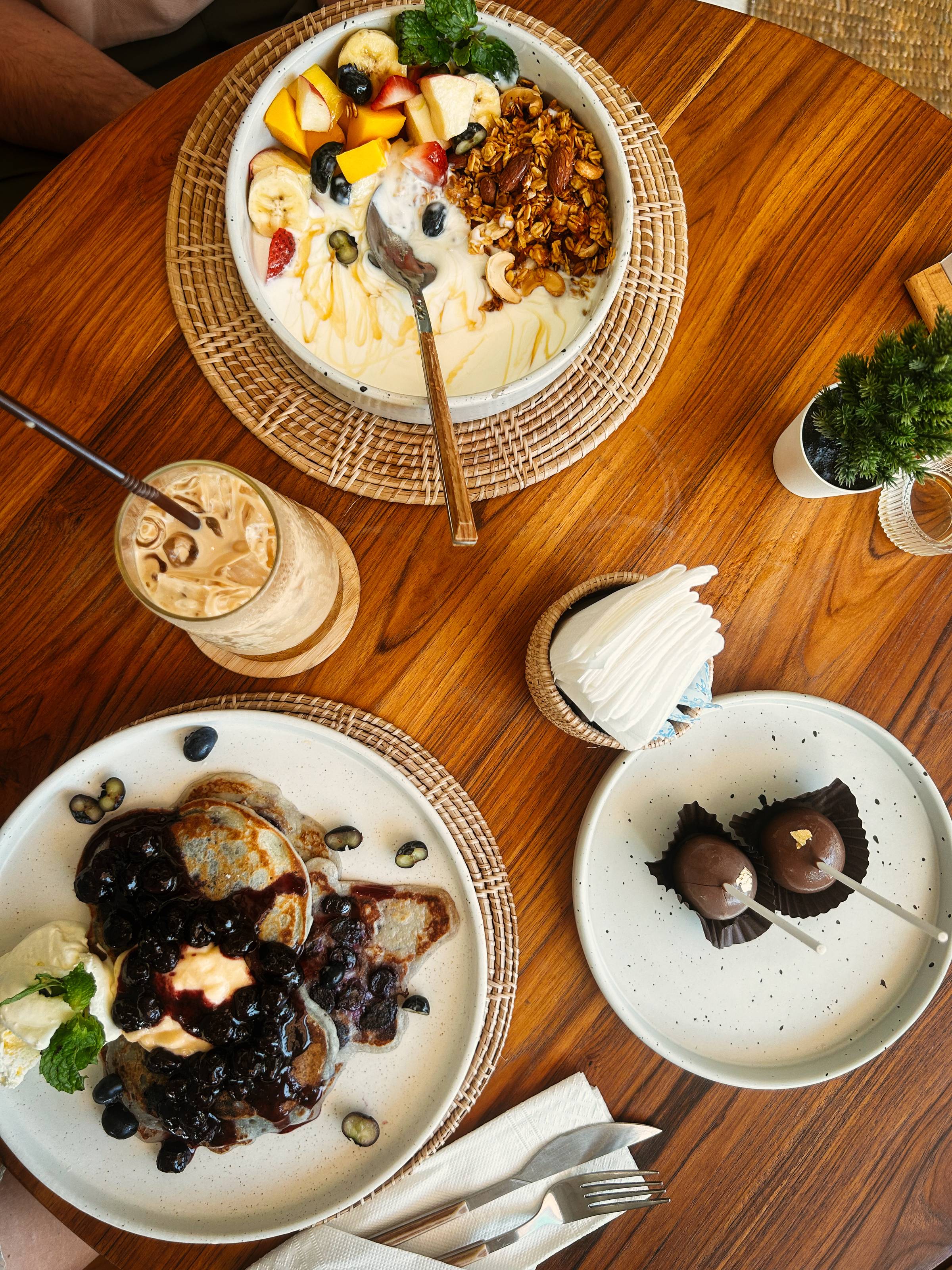 Birds eye view of a table with blueberry pancakes, granola, yoghurt and granola, cake pops and iced coffee