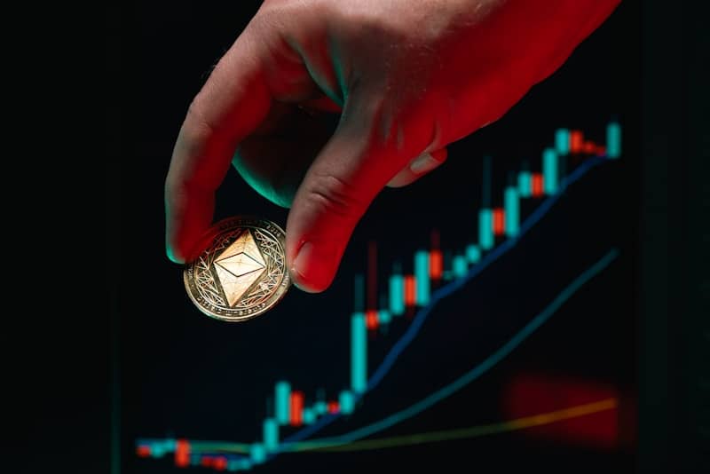 Hand holds ethereum coin over the stock chart.
