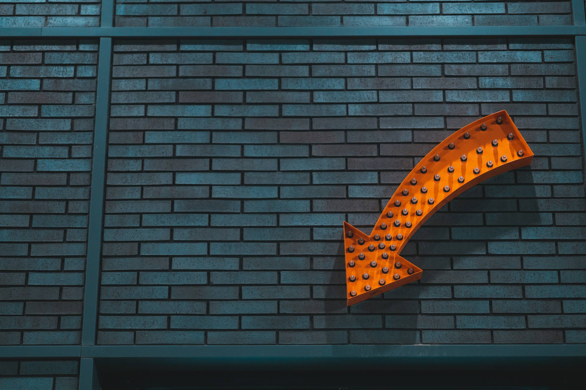 Orange arrow pointed down attached to a blue brick wall.