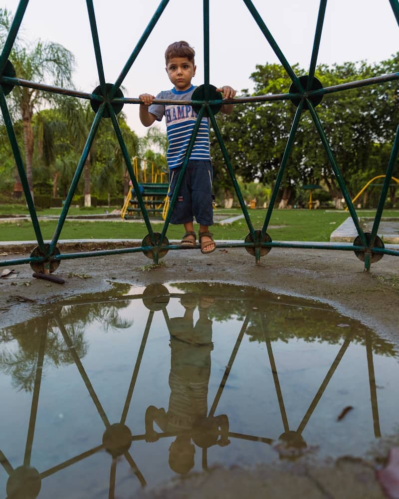 Young boy standing near a jungle gym with reflection