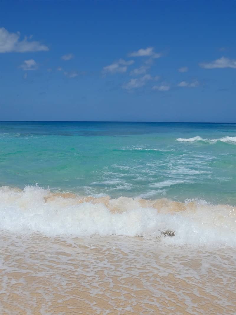 Waves crashing on a sandy beach under blue sky.