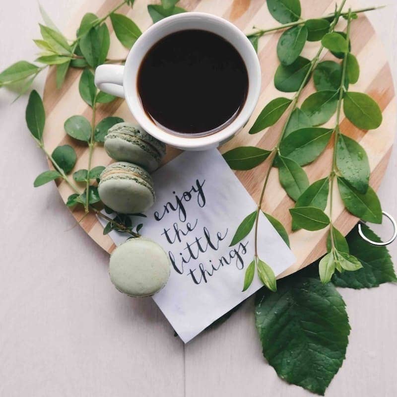 flat lay photography of leaves with cup of coffee and three macarons on chopping board