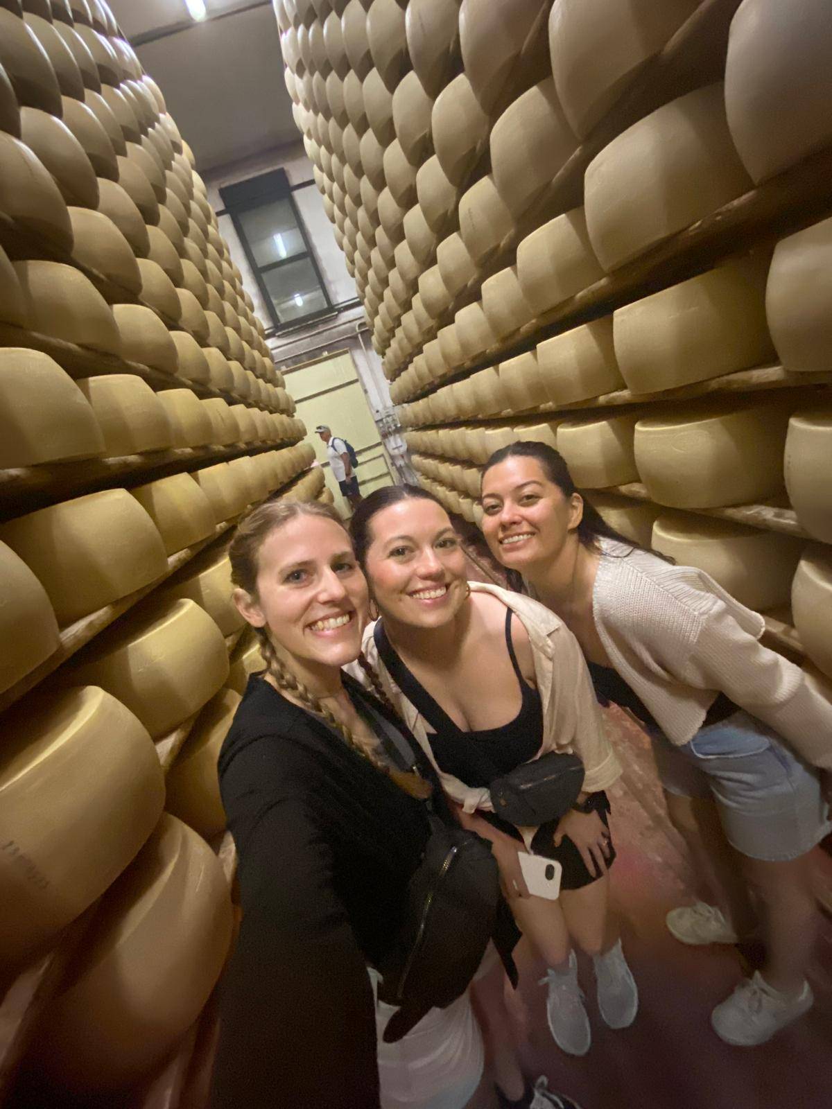 three girls standing next to cheese wheels.