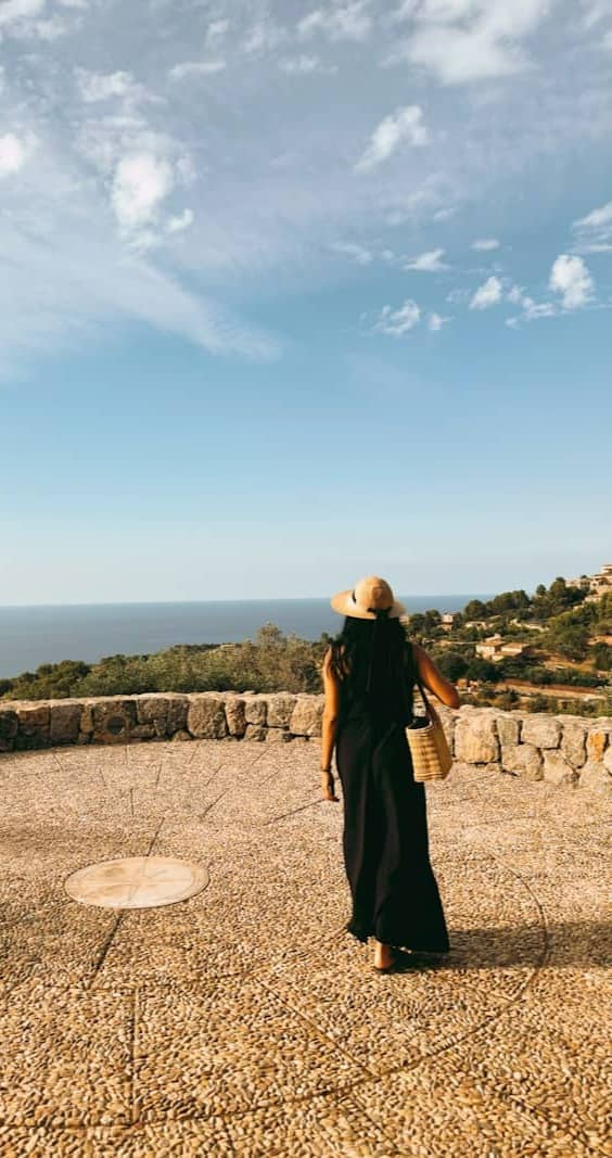Woman in straw hat overlooks ocean from stone terrace