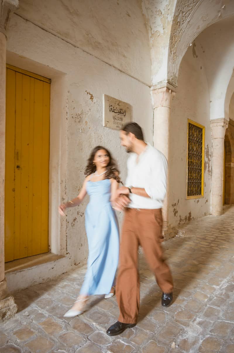 A woman in a blue dress and a man in a white shirt walking through a stone archway