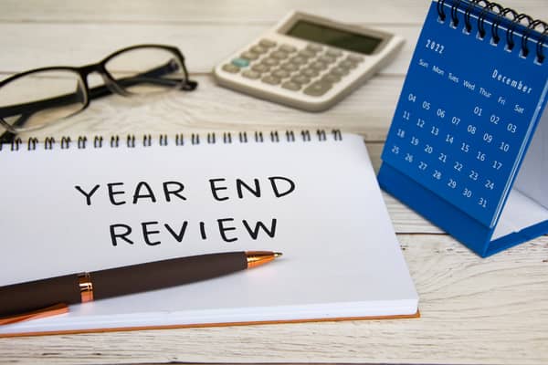 Photo of pen, paper, glasses, calculator, calendar and  with writing on paper that says year end review.