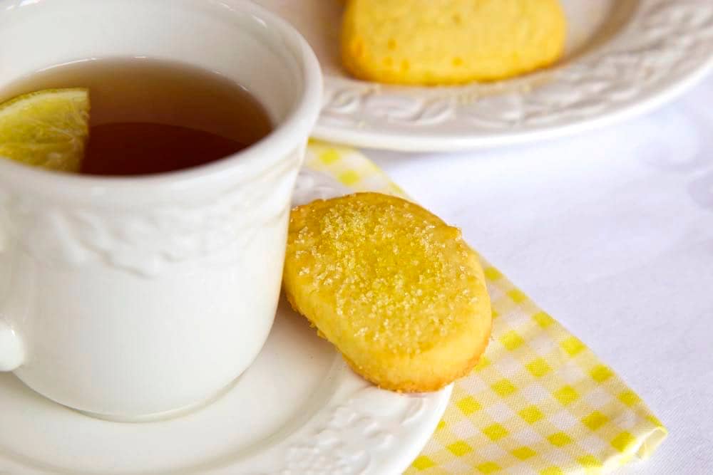 A cup of Early Grey tea with lemon, a piece of lemon shortbread is sitting on its saucer.