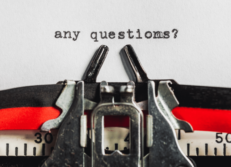 A close-up of a typewriter with a white piece of paper inside. The typewriter has just written the words 'any questions?'