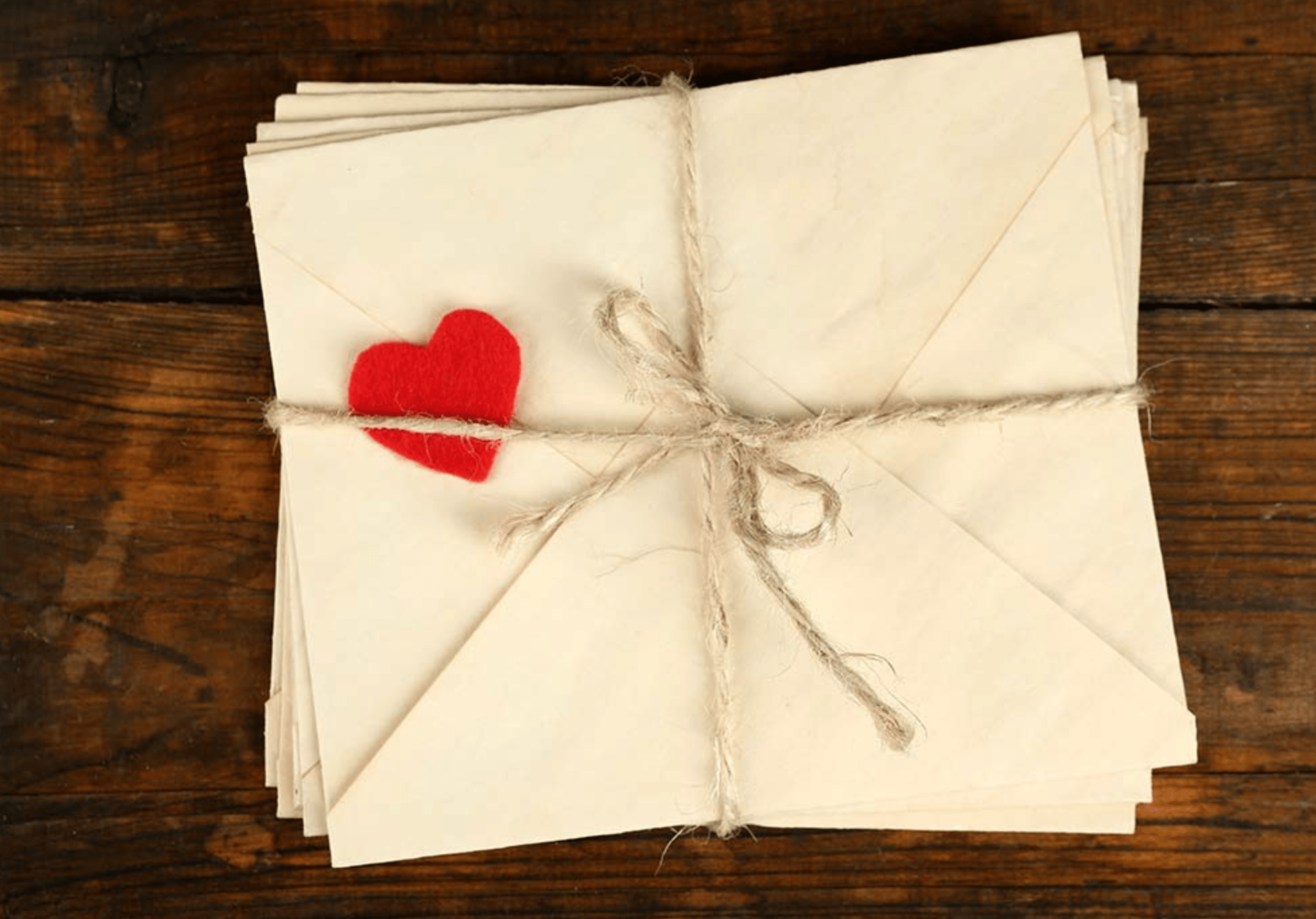 A stack of white envelopes tied in a bow with a piece of twine. A red felt heart sits on top of the topmost envelope.