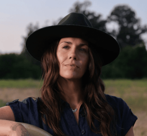 Image of Kristina in a field wearing a hat, smling. 