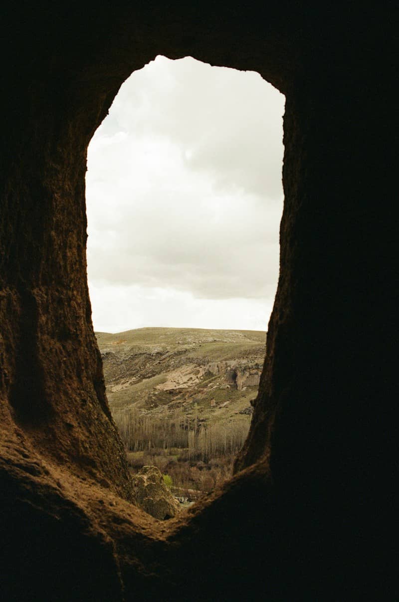 A view of a rocky valley and trees through a dark cave opening