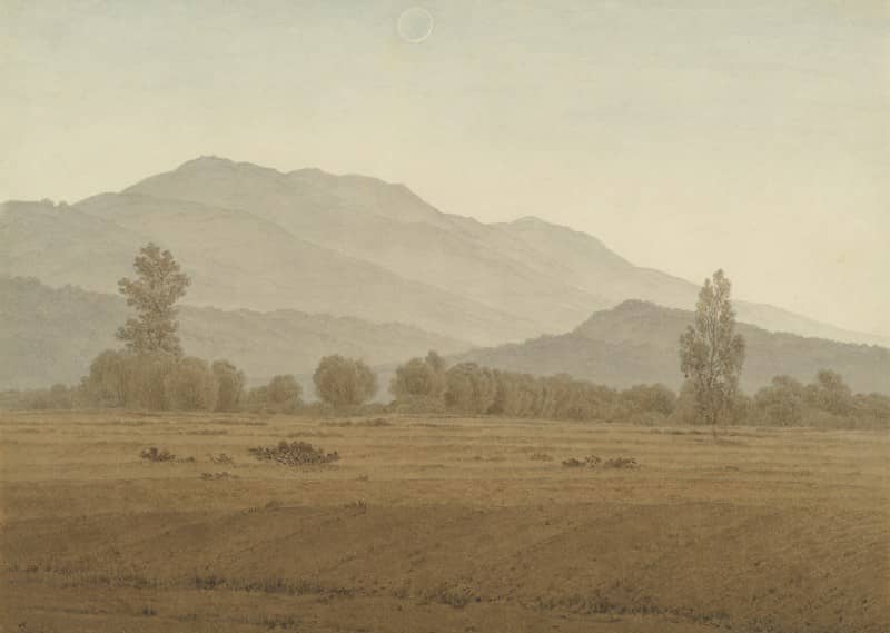 Misty mountains rise behind a field and trees