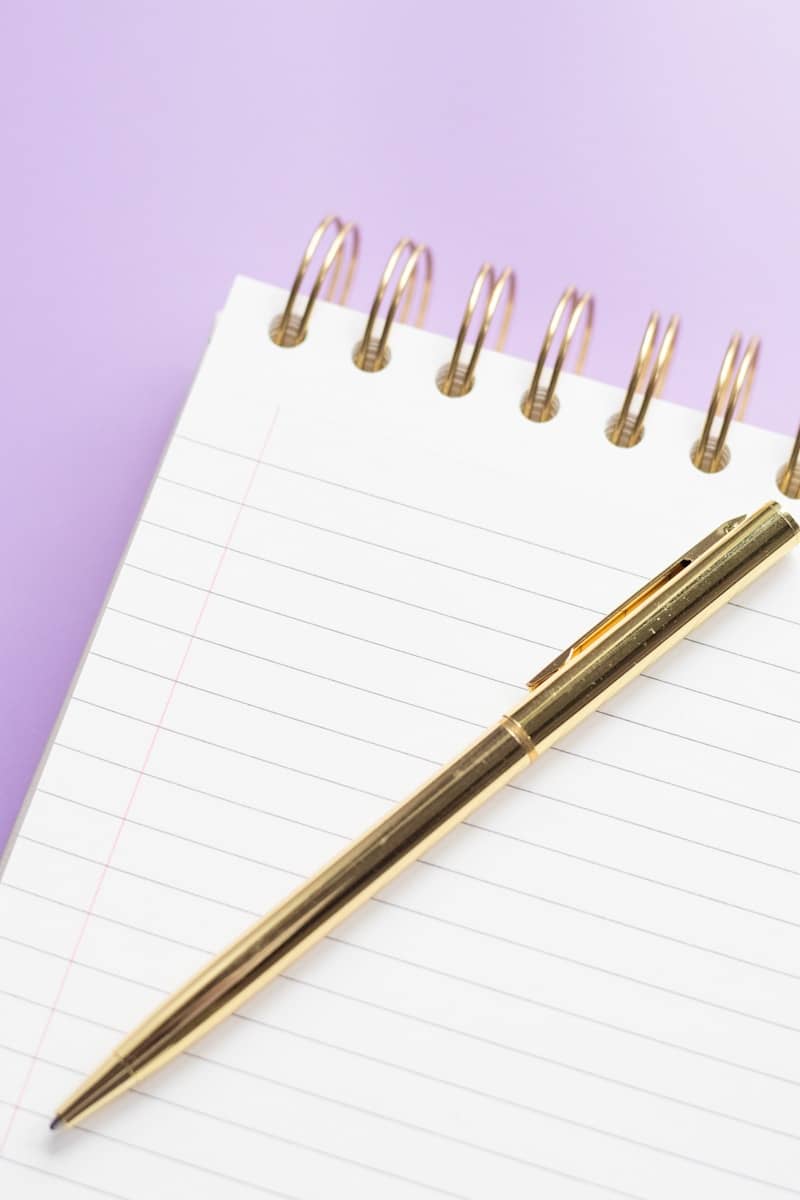 Golden pen rests on a lined spiral notebook.