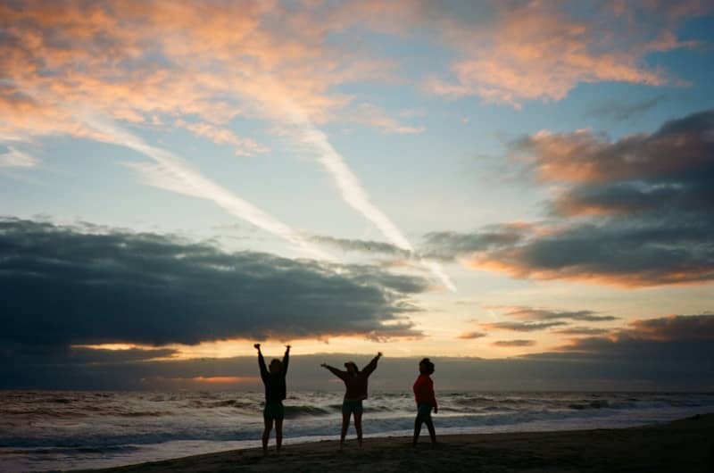 Three children celebrate on a beach at sunset.