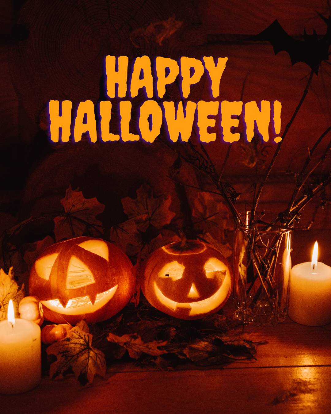 A dark background with shades of black, gray and orange with lit candles and jack o lanterns, some autumn leaves and twigs in a vase.